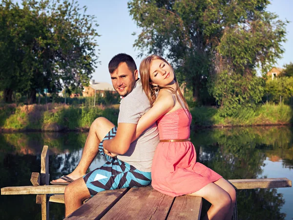 Joven pareja sentado abrazando en el puente por el río —  Fotos de Stock