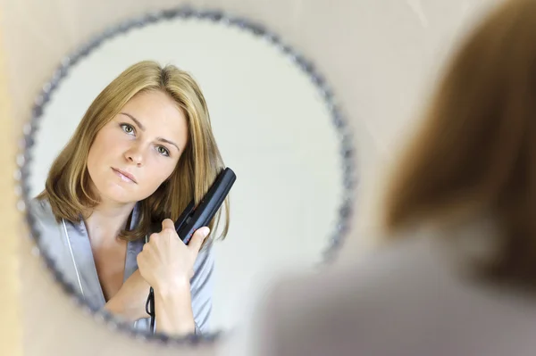 Beautiful young woman doing hair with iron — Stock Photo, Image