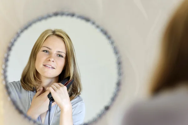 Beautiful young woman doing hair with iron — Stock Photo, Image