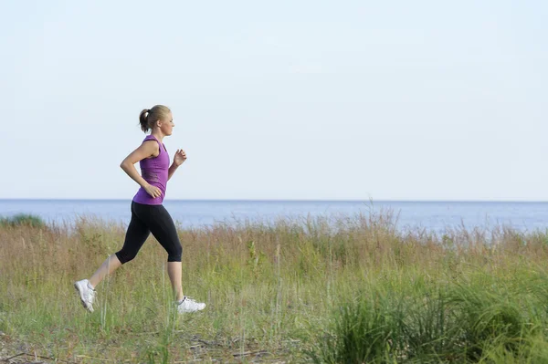 Ung kvinna löper längs sjöstranden — Stockfoto