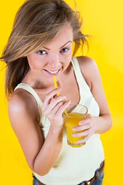 Menina adolescente bebendo suco de laranja no fundo amarelo — Fotografia de Stock
