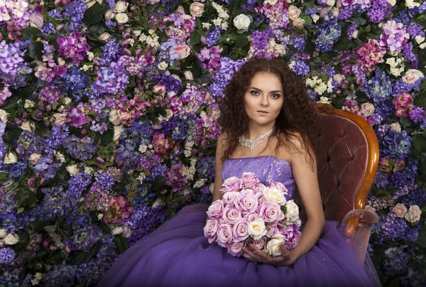 Retrato de uma menina bonita em um vestido roxo em um fundo de flores — Fotografia de Stock