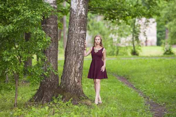 Tjej i klänning står nära ett träd i parken — Stockfoto