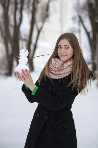 女孩穿件黑色的大衣，拿着一个雪人 — 图库照片