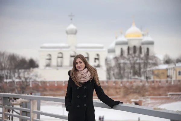 Россия. Девушка в черном пальто стоит на фоне Кремля в Великом Новгороде — стоковое фото