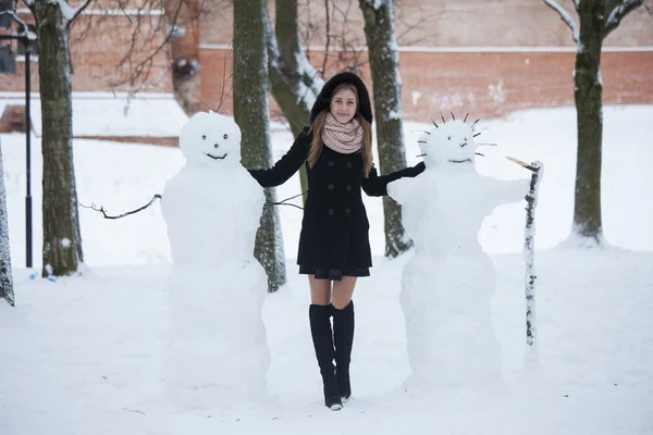 俄罗斯。俄罗斯的冬天。在黑色的外套站在两堆雪人的女孩 — 图库照片