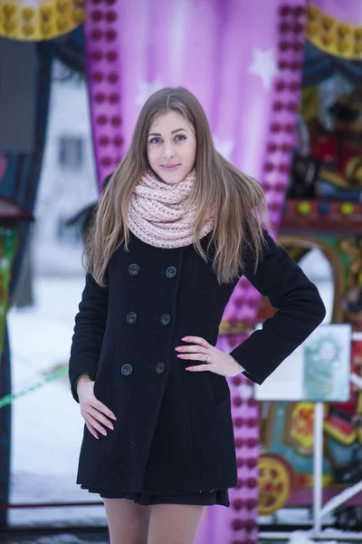 Девушка в черном пальто на фоне карусели — стоковое фото