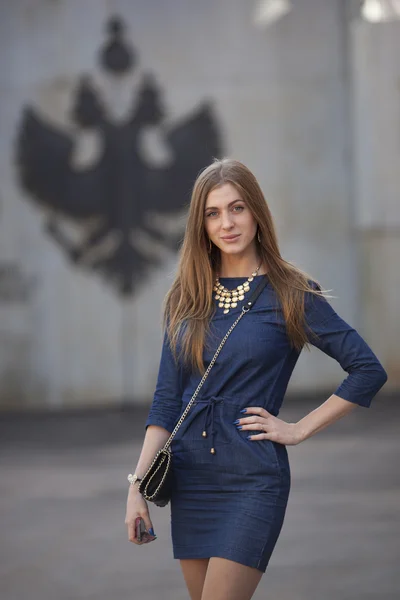 Mädchen in einem blauen Kleid steht auf dem Hintergrund Emblem von Russland — Stockfoto