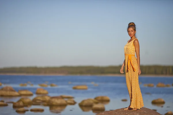 Niña con un vestido amarillo de pie sobre las rocas en la orilla del Golfo — Foto de Stock