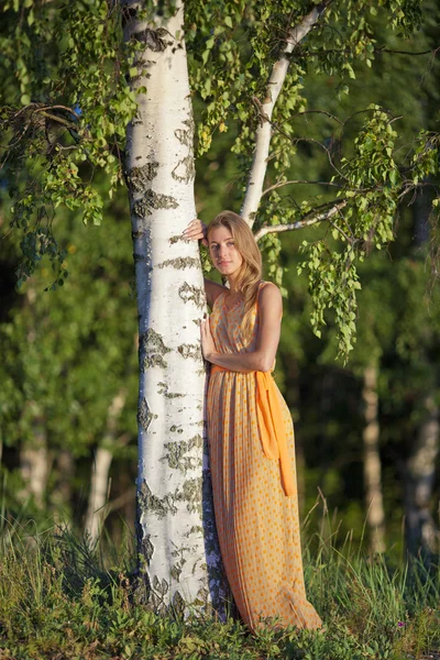 Niña en un vestido amarillo de pie en el abedul — Foto de Stock