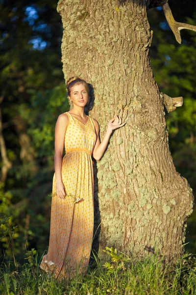 Jeune fille dans une robe jaune debout à l'arbre avec une fleur dans les mains — Photo