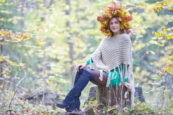 Autunno femminile. Giovane ragazza con una corona di foglie sulla testa seduta su un ceppo nel parco — Foto Stock