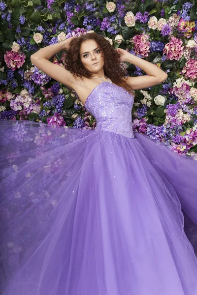 Retrato de una hermosa niña en un vestido púrpura sobre un fondo de flores —  Fotos de Stock