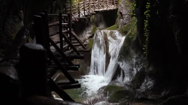 Дивовижні водоспади в скелястій ущелині, повній рослинності з дерев'яною доріжкою — стокове відео