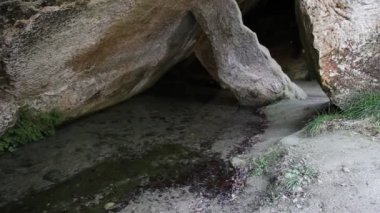 Bir mağaranın içindeki küçük bir göle yakınlaşırken kaya sütunlarıyla desteklenen bir mahzen.