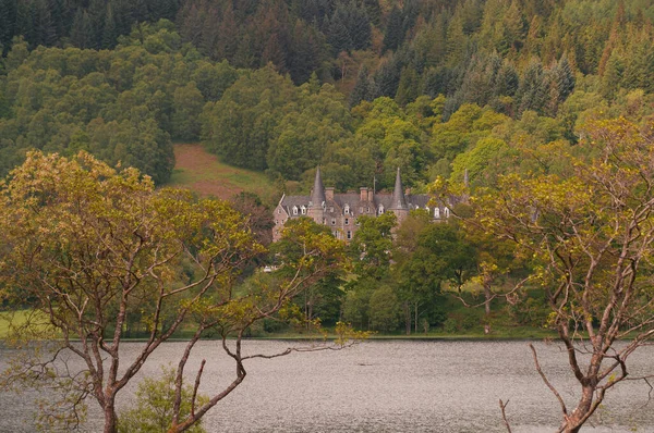 Antigua mansión de Mor Trossachs, frente al lago Achray, visible detrás de los árboles —  Fotos de Stock