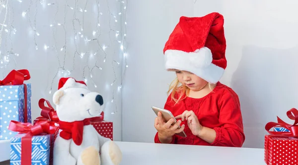 Поздравления в Интернете. Маленькая девочка в шляпе Санты с подарками. Звони бабушке и дедушке на Рождество.. — стоковое фото