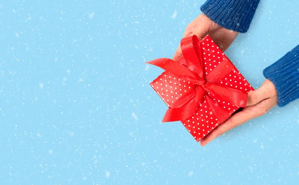 Manos está sosteniendo un regalo rojo en fondo azul con nieve. —  Fotos de Stock