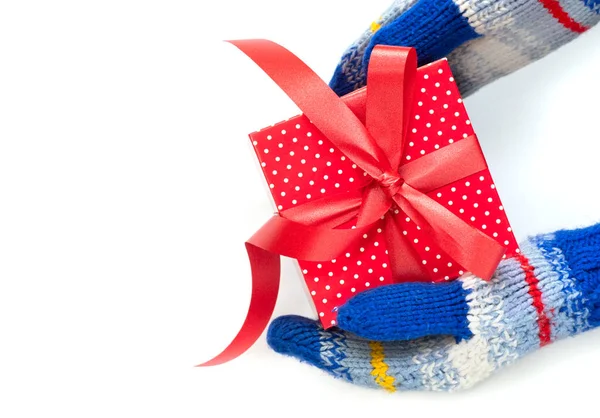 Manos en manoplas rayadas azules sostiene un regalo de Navidad rojo aislado en blanco. —  Fotos de Stock