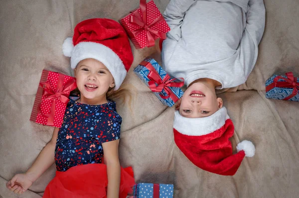 Дети в шляпе Санты лежат возле рождественских подарков и улыбаются. — стоковое фото