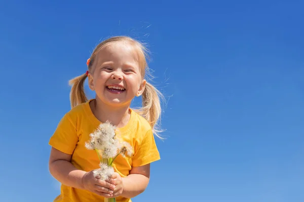 Uma menina encantadora com dentes-de-leão está rindo contra o céu azul. Verão ensolarado criança. — Fotografia de Stock