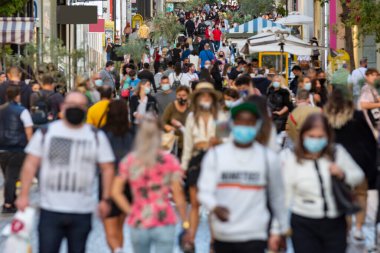 Kalabalık, kovid19 için koruyucu bir maske takarak alışveriş caddesinde bir aşağı bir yukarı dolaşıyor.