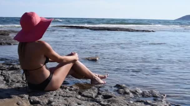 戴着红帽子 身穿黑色比基尼的漂亮女人沉着冷静地看着大海 夏日度假的概念 侧面风景 — 图库视频影像