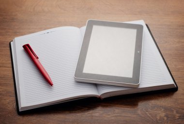 Tablet cihaz üstünde tahta masada açık defter