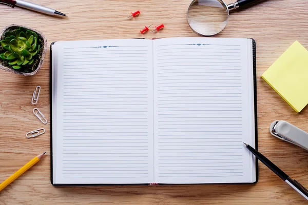 Papelería, bloc de notas abierto y una maceta en la mesa — Foto de Stock