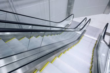 High-angle shot shows two glass and metal escalators moving down into a spacious, minimalist building interior.