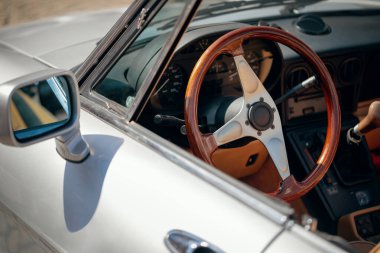 Eski bir arabanın içini detaylı bir şekilde görmek, ahşap ve metal direksiyonu ve yan aynayı gösteriyor..