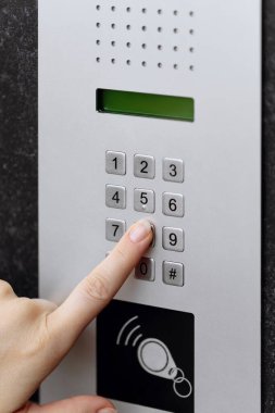Koyu dokulu bir duvara monte edilmiş modern bir dahili telefon tuş takımının düğmesine basan bir elin yakın çekimi.