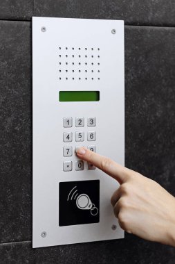 Koyu dokulu bir duvara monte edilmiş modern bir dahili telefon tuş takımının düğmesine basan bir elin yakın çekimi.