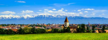 Baharda Sibiu şehrinin panoramik manzarası, karla kaplı Fagaras dağları, Romanya 'nın Karpat dağlarının bir kısmı