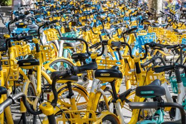 Şangay, Çin - 25 Eylül 2025 bisiklet paylaşım sistemi bisikletleri, Şangay, Çin. Güneşli bir günde düzgün park edilmiş sarı ve mavi renkli bisiklet sıraları.