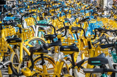 Şangay, Çin - 25 Eylül 2025 bisiklet paylaşım sistemi bisikletleri, Şangay, Çin. Güneşli bir günde düzgün park edilmiş sarı ve mavi renkli bisiklet sıraları.