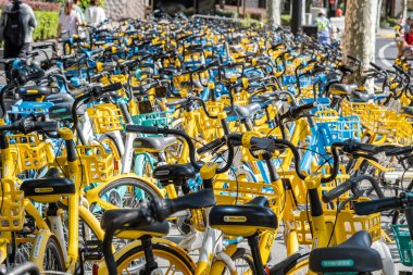 Şangay, Çin - 25 Eylül 2025 bisiklet paylaşım sistemi bisikletleri, Şangay, Çin. Güneşli bir günde düzgün park edilmiş sarı ve mavi renkli bisiklet sıraları.