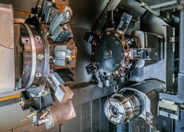 Çok sayıda civata ve dişlilere sahip çoklu dairesel metal bileşenlerden oluşan karmaşık bir endüstriyel makine. Makine parçaları ağırlıklı olarak siyah ve gri, gümüş aksanlı.