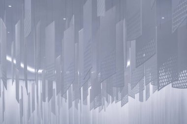 Tavandan sarkan bir dizi geometrik desenli kağıt fener. Fenerler, şebeke benzeri bir dizaynla dikdörtgen şeklindedir. Beyaz, hafif ışıklandırılmış arka plan üzerine karmaşık gölgeler bırakırlar.