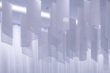 Tavandan sarkan bir dizi geometrik desenli kağıt fener. Fenerler, şebeke benzeri bir dizaynla dikdörtgen şeklindedir. Beyaz, hafif ışıklandırılmış arka plan üzerine karmaşık gölgeler bırakırlar.