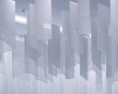 Tavandan sarkan bir dizi geometrik desenli kağıt fener. Fenerler, şebeke benzeri bir dizaynla dikdörtgen şeklindedir. Beyaz, hafif ışıklandırılmış arka plan üzerine karmaşık gölgeler bırakırlar.