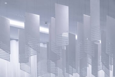 Tavandan sarkan bir dizi geometrik desenli kağıt fener. Fenerler, şebeke benzeri bir dizaynla dikdörtgen şeklindedir. Beyaz, hafif ışıklandırılmış arka plan üzerine karmaşık gölgeler bırakırlar.