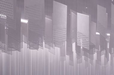 Tavandan sarkan bir dizi geometrik desenli kağıt fener. Fenerler, şebeke benzeri bir dizaynla dikdörtgen şeklindedir. Beyaz, hafif ışıklandırılmış arka plan üzerine karmaşık gölgeler bırakırlar.