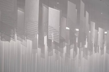 Tavandan sarkan bir dizi geometrik desenli kağıt fener. Fenerler, şebeke benzeri bir dizaynla dikdörtgen şeklindedir. Beyaz, hafif ışıklandırılmış arka plan üzerine karmaşık gölgeler bırakırlar.