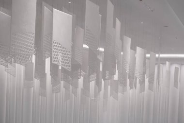 Tavandan sarkan bir dizi geometrik desenli kağıt fener. Fenerler, şebeke benzeri bir dizaynla dikdörtgen şeklindedir. Beyaz, hafif ışıklandırılmış arka plan üzerine karmaşık gölgeler bırakırlar.