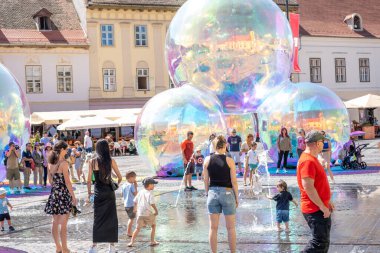 Sibiu, Romanya - 25 Haziran 2025 Sıcak bir yaz gününde şehir meydanında küçük fıskiyelerle oynayan çocuklar