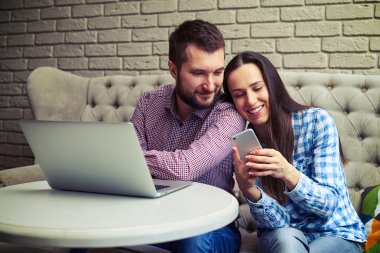 gülen genç çift kanepede oturan gadget'lar ile 