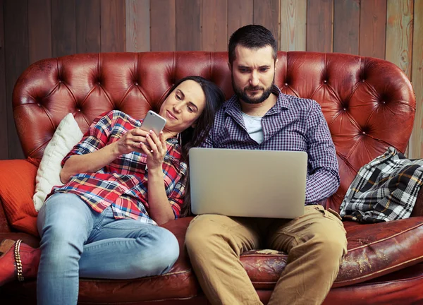 Couple assis sur le canapé et utilisant des gadgets — Photo