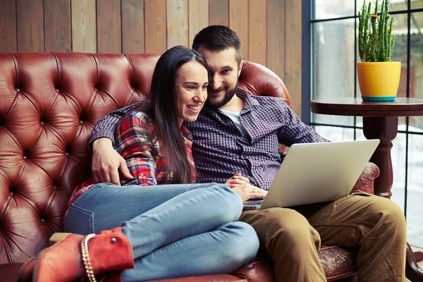 Пара, сидящая на диване и использующая ноутбук дома — стоковое фото