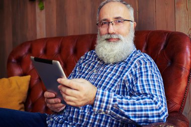 tablet pc ile kanepede oturan ve kameraya bakarak adam